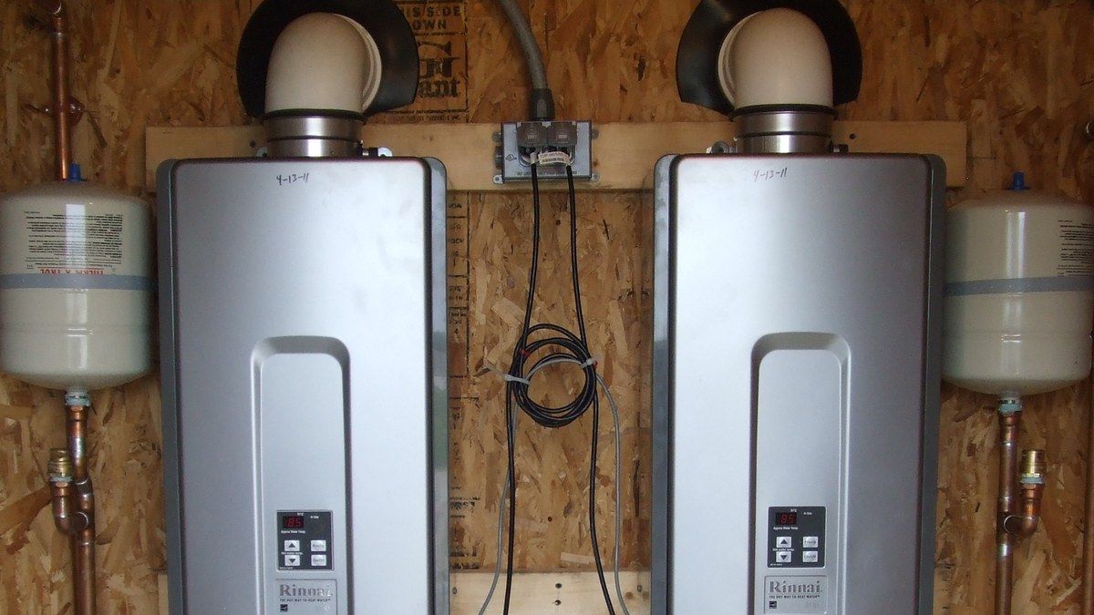 Two commercial condensing tankless water heaters mounted side by side in a utility room.
