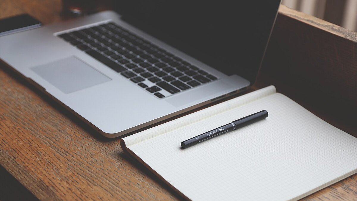A laptop and a notebook on a wooden desk, the setup an owner uses when deciding whether to have a real website built